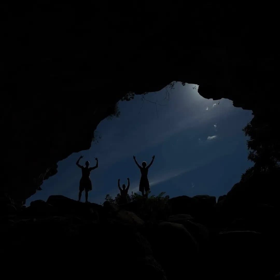 Tres personas en silueta en la entrada de una cueva, contraluz azul